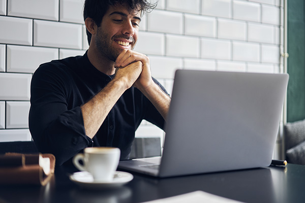 Man sits smiling at laptop, with a mug next to it.